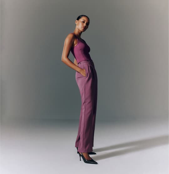 Model is wearing purple tank top and purple straight-leg pants.